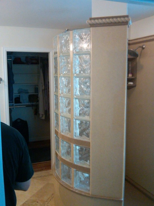A curved glass block shower wall integrated into a beige tiled pillar during a bathroom renovation.