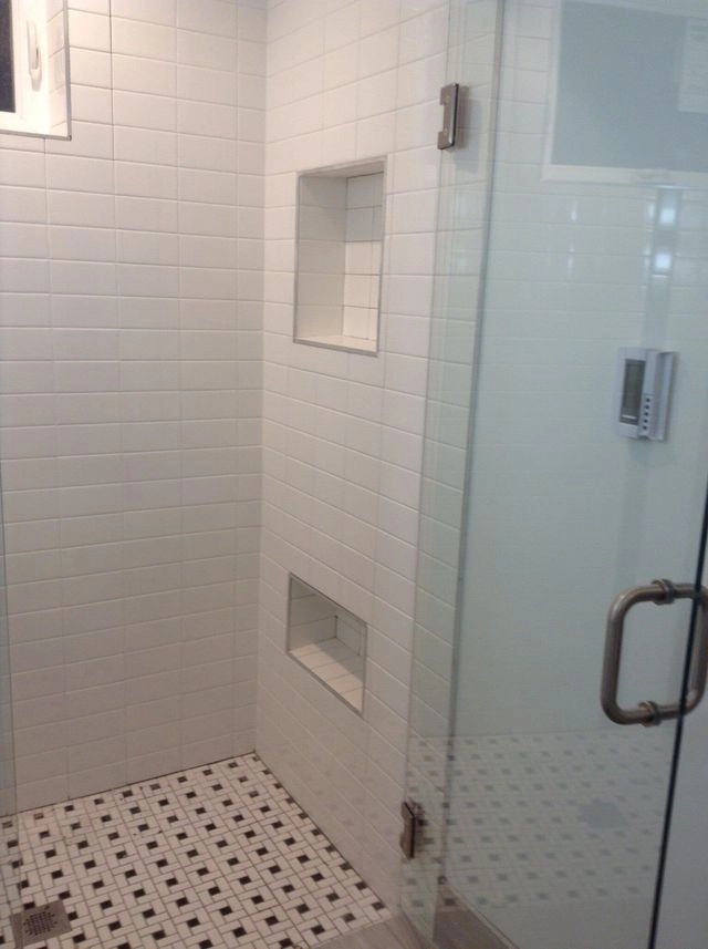 Modern walk-in shower with white subway tiles, two recessed wall niches, and a black and white mosaic tile floor.
