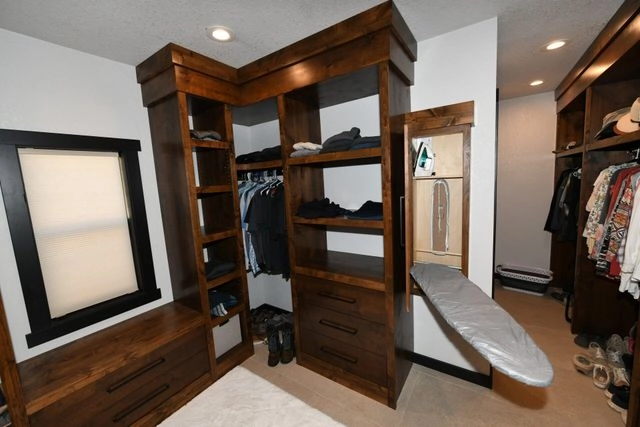 Custom dark wood walk-in closet with built-in shelving, drawers, and a fold-out ironing board.