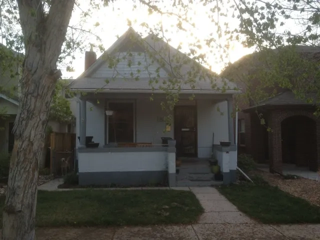 A small white residential house with a front porch before undergoing major renovations.