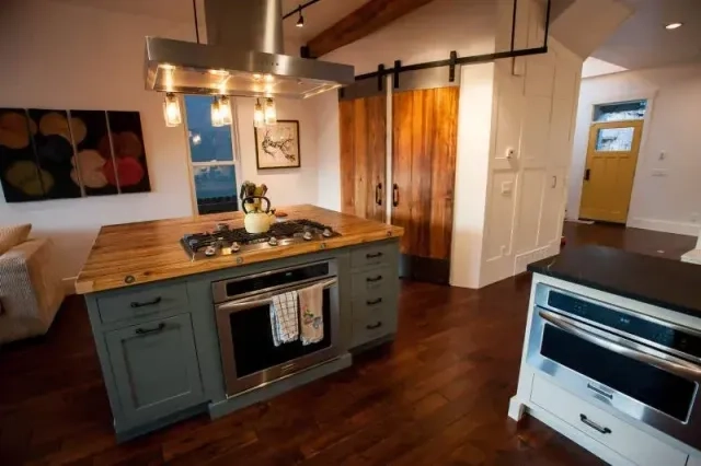 Modern rustic kitchen renovation featuring a sage green island with butcher block top and sliding wood barn doors.